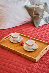Cozy morning: tray with teacups on red quilt in bedroom setting