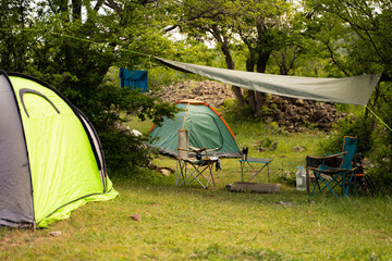 Two tourist camping tents with chairs and table in nature with green forest and grass among a trees on a background, eco tourism and outdoor equipment for hiking