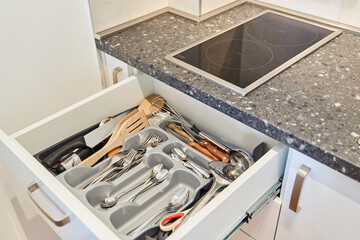 Organized kitchen drawer with cutlery and utensils near granite counter and induction cooktop