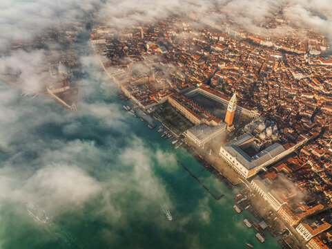 Aerial view of the iconic St. Mark's Square and Doge's Palace emerge from the ethereal mist, contrasting with the turquoise waters of the lagoon, Venice, Veneto, Italy.