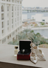 Luxury bridal shoes and engagement ring box on a balcony with a blurred hotel and palm view. A...