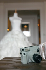 A vintage camera resting on a soft surface with a blurred wedding dress in the background. A...