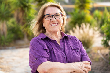A happy retired woman with crossed arms radiates joy and contentment smiling and enjoying a...