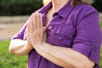 Close-up of a senior woman's hands practicing yoga and meditating with her hands in prayer position...