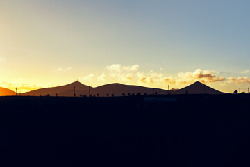 Golden hour silhouettes of volcanic peaks against a vibrant sunset sky. Mountain tops stand in...