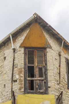 View of weathered stone building with a dilapidated wooden door and triangular ochre accent under a cloudy sky in Limassol, Limassol, Cyprus.