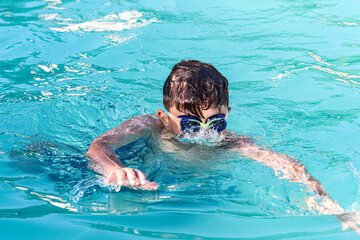 Child with glasses swimming in a pool.