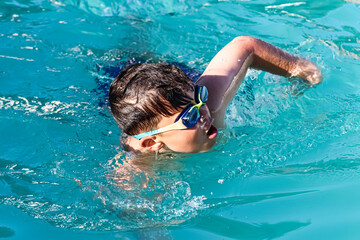 Child with glasses swimming in a pool.