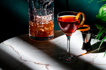 Elegant cocktail on a marble table with a pitcher and garnish, showcasing a refined drink in a chic setting