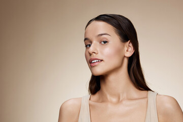 Elegant portrait of a confident young woman with long hair and a natural expression, set against a soft beige background highlighting her beauty and grace
