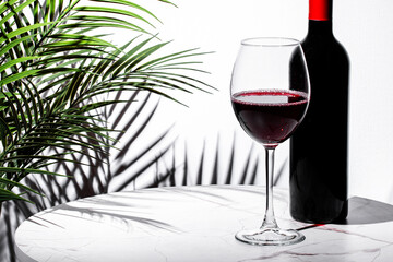 Elegant glass of red wine with bottle beside palm leaf shadow on a marble table in a luxurious setting