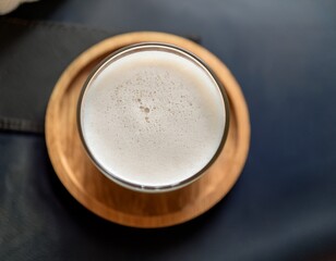 creamy delight a top down shot of a refreshing beverage a glass filled with a frothy light colored drink resting on a natural wooden coaster embodying a sense of serenity and sensory indulgence