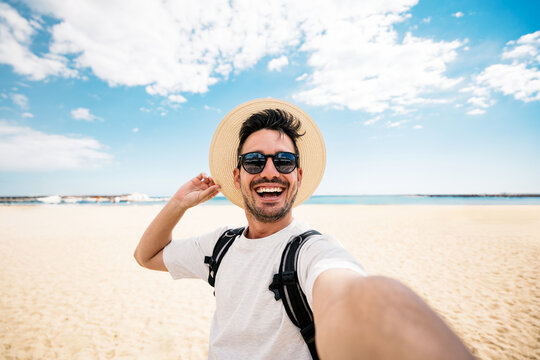 Handsome young man taking selfie picture at beach summer vacation - Smiling guy having fun walking outside - Summertime holidays and technology concept