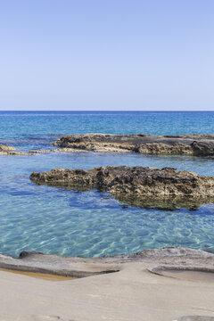 View of turquoise water gently washing over rocky shores under a clear blue sky, creating a serene coastal scene, Dipkarpaz, Northern Cyprus, Cipro.