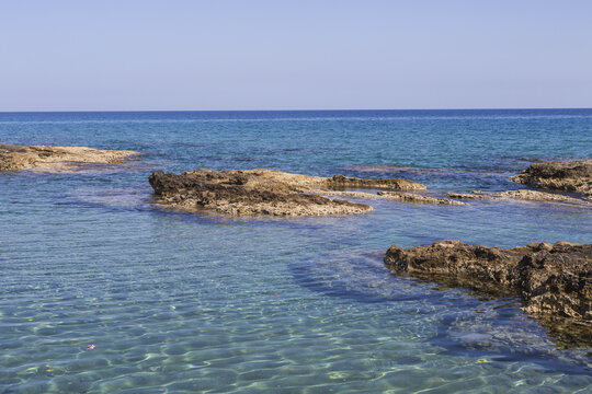View of tranquil, turquoise waters gently lap against rugged, dark rocks under a clear sky, a serene coastal scene, Dipkarpaz, Northern Cyprus, Cipro.