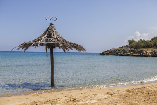 View of a weathered straw umbrella stands sentinel on the sandy shore, turquoise waters gently lapping, inviting tranquility, Dipkarpaz, Northern Cyprus, Cipro.