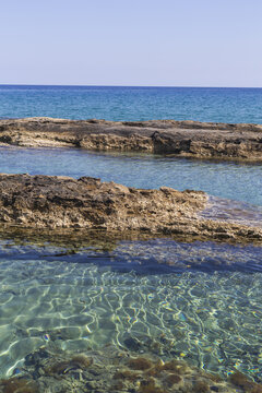 View of turquoise waters meet rugged, sun-baked rocks under a serene blue sky, creating a tranquil coastal scene, Dipkarpaz, Northern Cyprus, Cipro.
