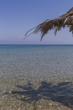 View of the serene, turquoise sea gently meeting the sun-kissed, sandy shore under a rustic straw parasol's shade, Dipkarpaz, Northern Cyprus, Cipro.