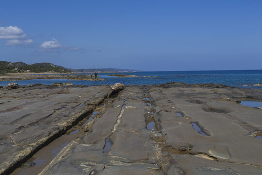 View of textured rock formations meet the turquoise sea under a clear blue sky, a tranquil coastal scene, Dipkarpaz, Northern Cyprus, Cipro.