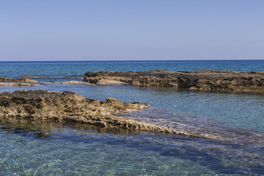 View of sun-kissed rocks meet the turquoise sea under a clear blue sky, creating a tranquil coastal scene, Dipkarpaz, Northern Cyprus, Cipro.