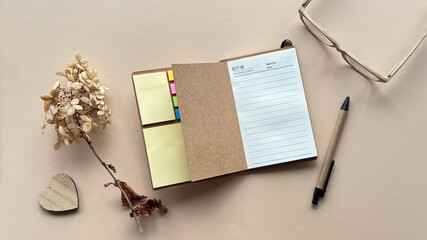Open notebook with sticky notes, pen, dried flowers, wooden heart, and glasses on beige background