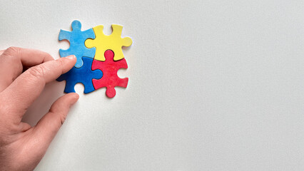 Hand holding colorful puzzle pieces symbolizing Autism Awareness on light background with copy-space
