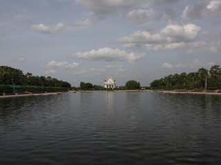 Fototapeta premium Reflecting temple architecture, this serene lake at Phutthamonthon captures a harmonious blend of nature and spiritual design, showcasing Thai artistry under dramatic skies.