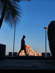 A silhouette of a man walking in front of the majestic 99 Domes Mosque in Makassar, Indonesia, under a clear blue sky. The perfect harmony of architecture, human activity, and natural light