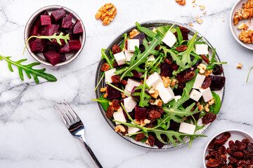Gourmet beet salad with soft cheese, arugula, raisins and walnuts, marble table background, top view