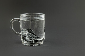 Water purification with black Shungite stone, clear drinking glass with stones on gray background. Removing toxins and organic matter from the water. Alternative lifestyle.