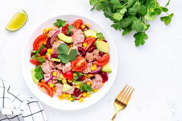Mexican style salad with canned tuna, avocado, corn, red beans, cherry tomatoes and cilantro, white table background, top view