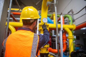 Engineer is checking pressure gauges on gas pipelines in a large factory