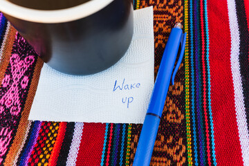 Coffee cup with a note written that says wake up on a colorful Inca woven table