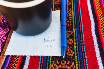 Coffee cup with a note written that says wake up on a colorful Inca woven table