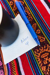 Coffee cup with a note written that says wake up on a colorful Inca woven table