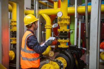 Engineer is checking pressure gauges on large gas pipelines inside a plant
