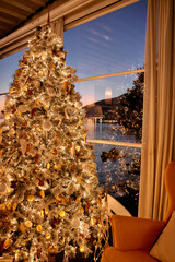 Festive christmas tree by cozy lakeside window at dusk with sparkling lights and ornaments