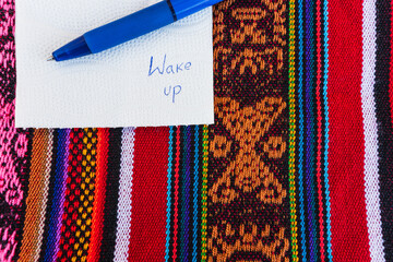 Coffee cup with a note written that says wake up on a colorful Inca woven table