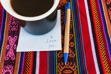 Coffee cup with a note written that says I love you on a colorful Inca woven table