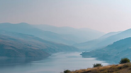 **Minimalist view of a tranquil lake bordered by gentle hills and a pale blue sky with haze