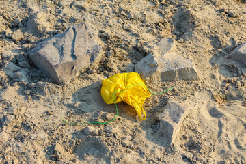 Bright yellow crumpled paper or plastic waste lying on sandy beach ground
