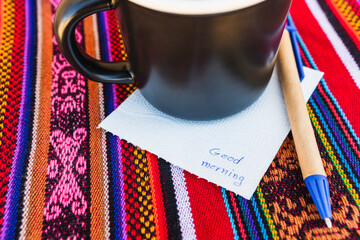 Coffee cup with a note saying good morning on a colorful table with Inca weave.