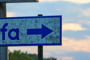 Blue directional arrow sign pointing right against cloudy sunset sky background