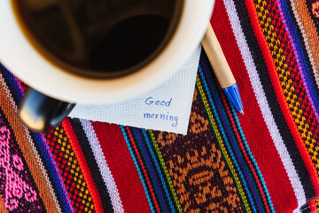 Coffee cup with a note saying good morning on a colorful table with Inca weave.