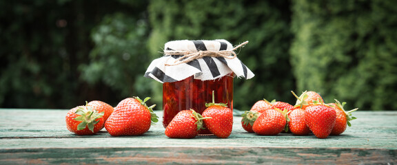 Fresh homemade strawberry jam in a jar with red berries on an old wooden table outdoors. Preserving...
