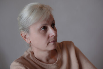 Close-up of a mature woman with light hair and earrings wearing a beige sweater, looking to the...