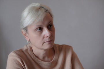 Portrait of a serious middle-aged woman with blonde hair looking thoughtfully to the side, wearing...