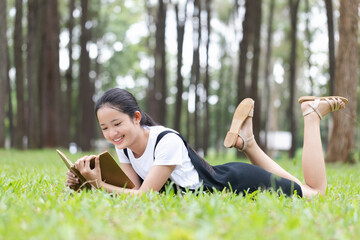 Smiling young girl lying on grass reading book in garden and admiring nature