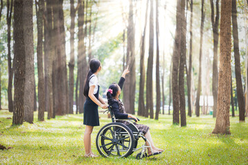 A woman in a wheelchair and her caregiver are watching the sunlight from the forest together