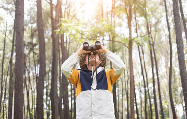 Male hiker standing looking through binoculars in green forest